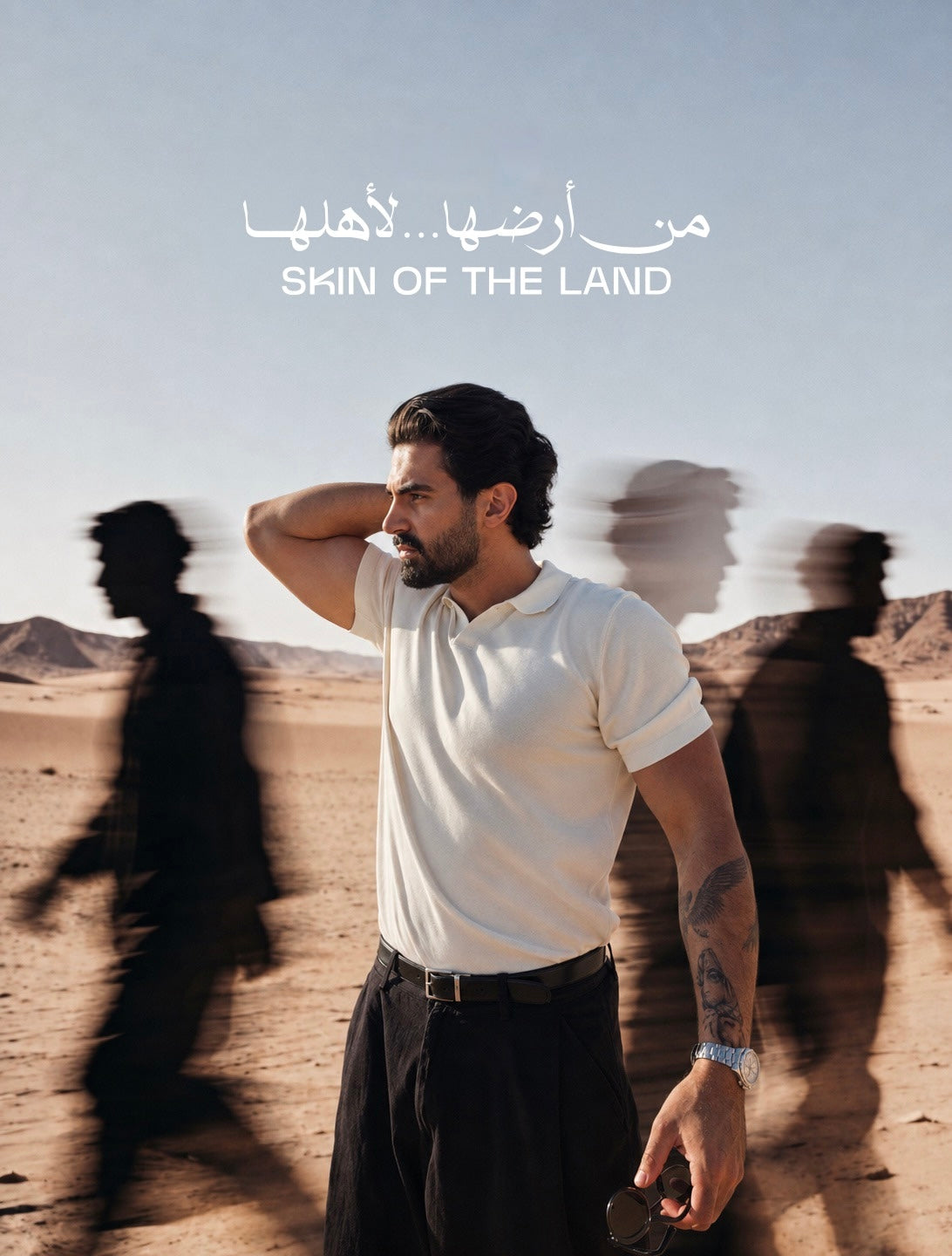 A man stands in a desert landscape wearing a white polo shirt and dark trousers, with Arabic text and the English phrase 'SKIN OF THE LAND' at the top. Motion-blurred shadow figures appear behind him against a pale blue sky.