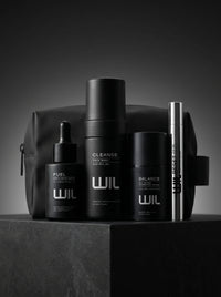 Full set of WIL products, including Cleanse face wash, Balance serum, Reset eye gel and Fuel hair and beard serum, arranged in front of WIL branded pouch on a dark gray pedestal against a dark gray background.